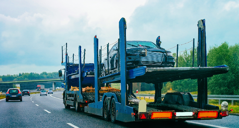 A high-tech car carrier transport truck moving through a digital toll plaza in 2026.